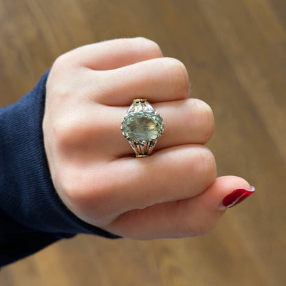 Hand wearing a ring with a green gemstone against a wooden background